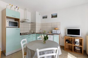 A kitchen with a dining table, chairs, a microwave, a stove, and a television on a wooden stand. - Gîte la Salamandre – In the Heart of the Loire Castles (Mosnes)