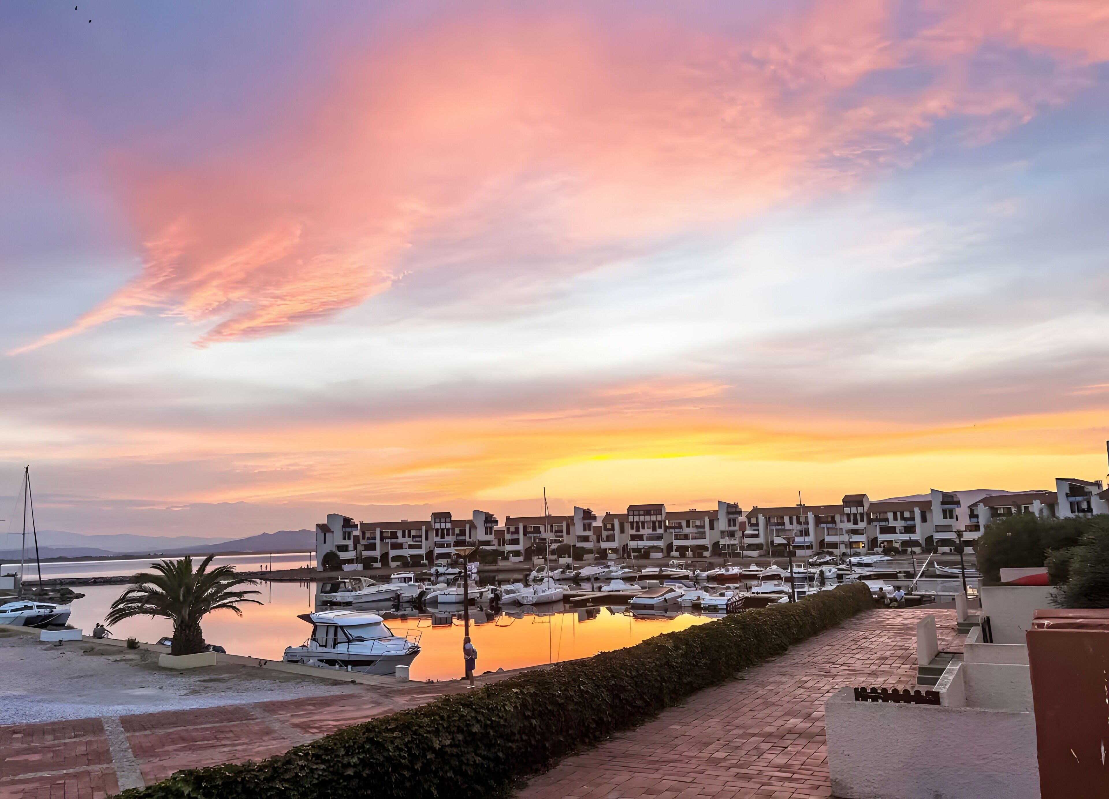 A marina with boats docked, a row of buildings, and a sunset sky. - Maison Goéland – A Relaxing Getaway Between Land and Sea, Shared Pool & Balcony (Le Barcarès)