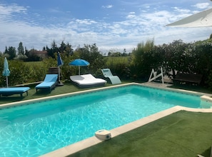 Une piscine entourée de verdure, avec des chaises longues et des parasols.