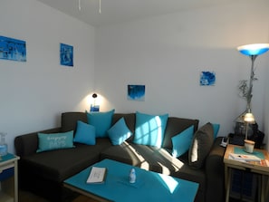Un salon moderne avec un canapé d’angle, une table basse, une lampe et des œuvres d’art accrochées aux murs.