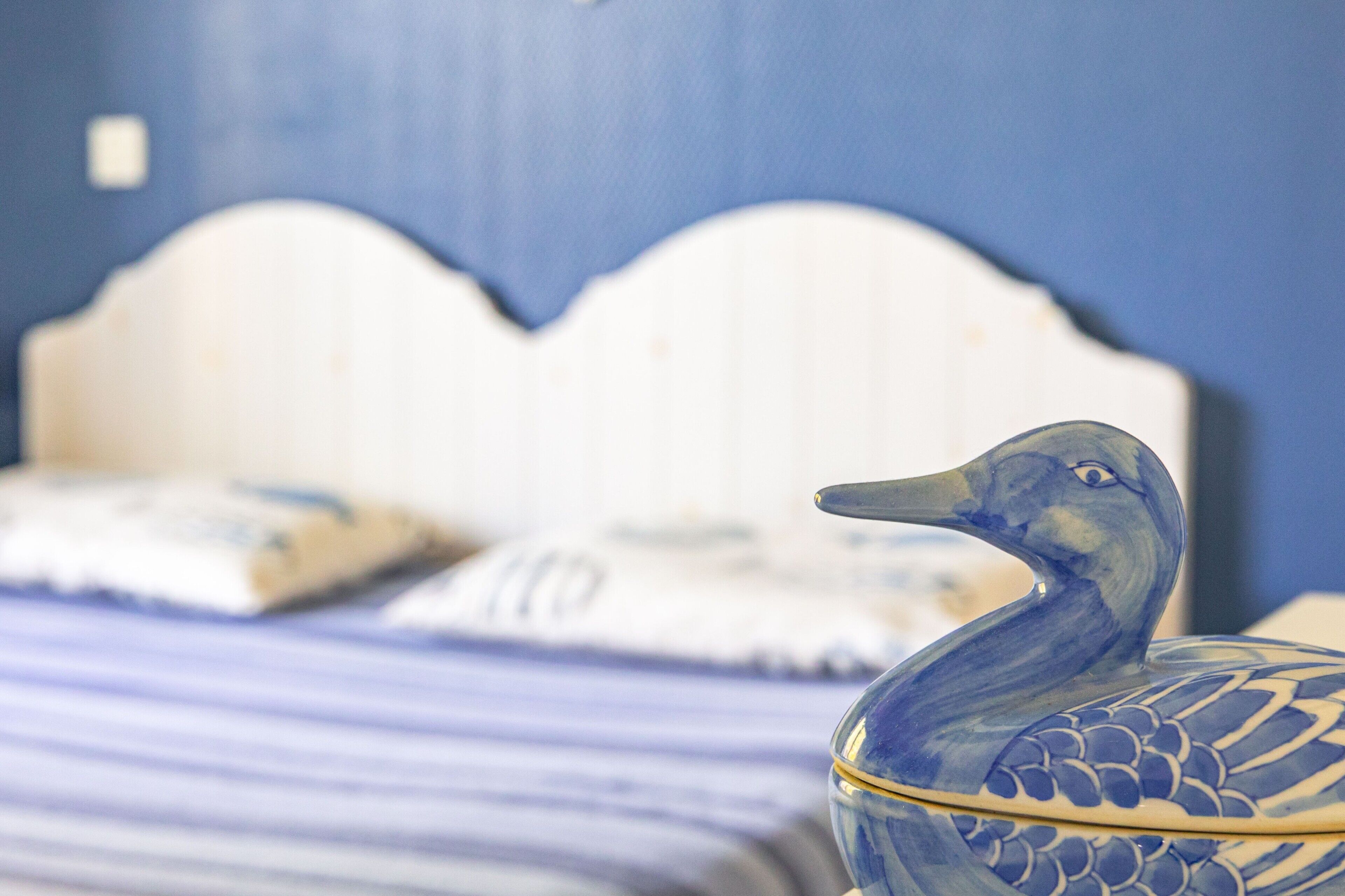 A bed with a white headboard, a blue ceramic duck-shaped container, and a striped pillow.