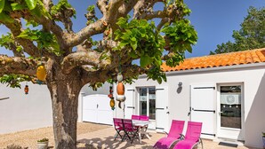 Un albero con ornamenti appesi, un edificio bianco con tetto in tegole, un tavolo con sedie e due poltrone.