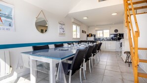 A dining area with a table set for six, a mirror, and a kitchen in the background. - Holiday Home 'L'escale bleue' with Shared Terrace, Private Garden & Wi-Fi (Plomeur)
