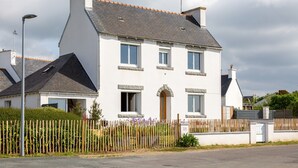 A two-story house with a white exterior, a dark roof, and a wooden fence in front. - Holiday Home 'L'escale bleue' with Shared Terrace, Private Garden & Wi-Fi (Plomeur)
