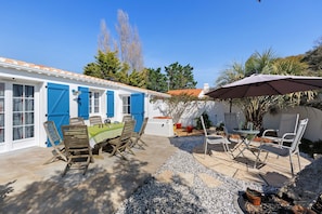 Une terrasse avec une table et des chaises, une porte bleue et un bâtiment blanc.