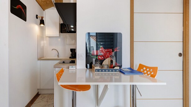 A compact kitchen with a white countertop, a sink, and a small dining area with a table and two chairs.