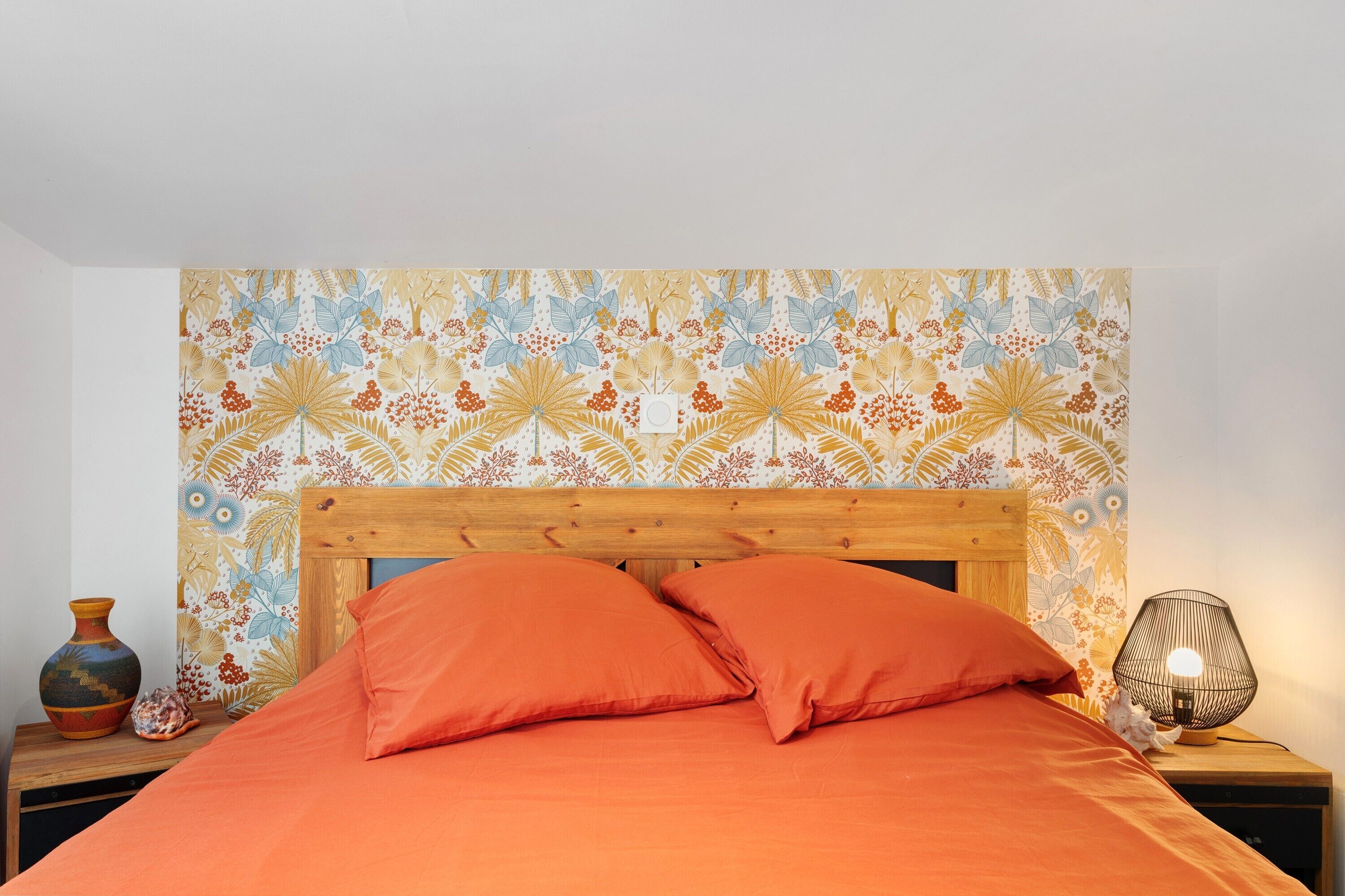 Un lit avec une literie orange, une tête de lit en bois et une table de chevet avec une lampe.