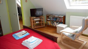 Une chambre à coucher avec un lit, une télévision, une bibliothèque, une chaise et une fenêtre.