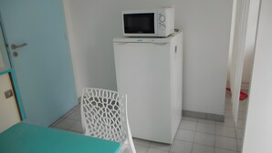 Une petite pièce comprenant un micro-ondes posé sur un petit meuble blanc, une table turquoise et une chaise blanche.