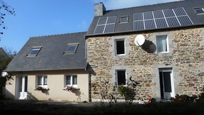 Ein Gebäude aus Stein mit geneigtem Dach, Solaranlagen und einer Satellitenschüssel.