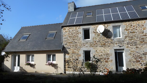 Un bâtiment en pierre avec un toit en pente, des panneaux solaires et une antenne parabolique.