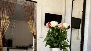 Un coin repas avec une table ronde en verre, un vase blanc orné de fleurs, une cuisine en arrière-plan et un sol à motifs.
