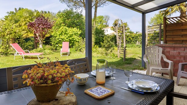 Une terrasse extérieure avec une table dressée pour le repas, une plante en pot et une vue sur le jardin.