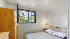 Une chambre à coucher avec un lit, une armoire en bois, une fenêtre et une lampe fixée au mur.