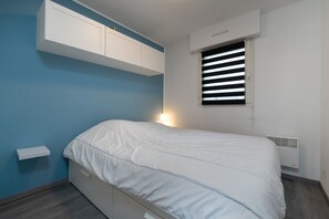 A bedroom with a bed, a window with blinds, a wall-mounted cabinet, and a bedside table. - Sailing, port, near beach & Thalasso, parking, towels & cleaning not included (Arzon)
