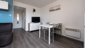 A modern living room with a sofa, a dining table with chairs, a TV, and a painting on the wall. - Sailing, port, near beach & Thalasso, parking, towels & cleaning not included (Arzon)