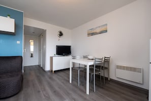 A modern living room with a sofa, a dining table with chairs, a TV, and a painting on the wall. - Le Sailing Apartment: Port View, Near Beach & Thalasso, Private Parking (Arzon)