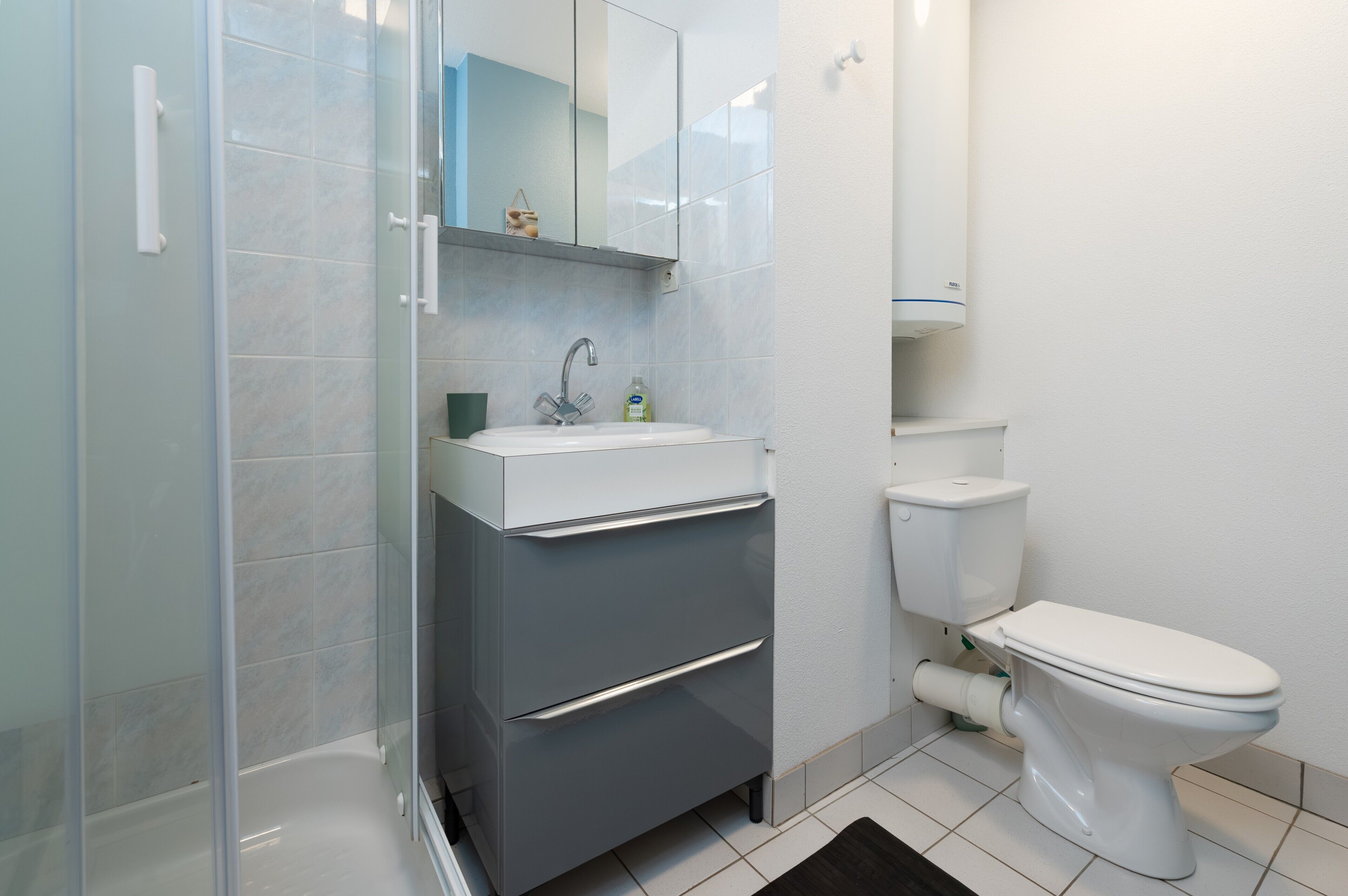 Een badkamer met een douchecabine van glas, een witte wastafel met een spiegel erboven en een wit toilet.