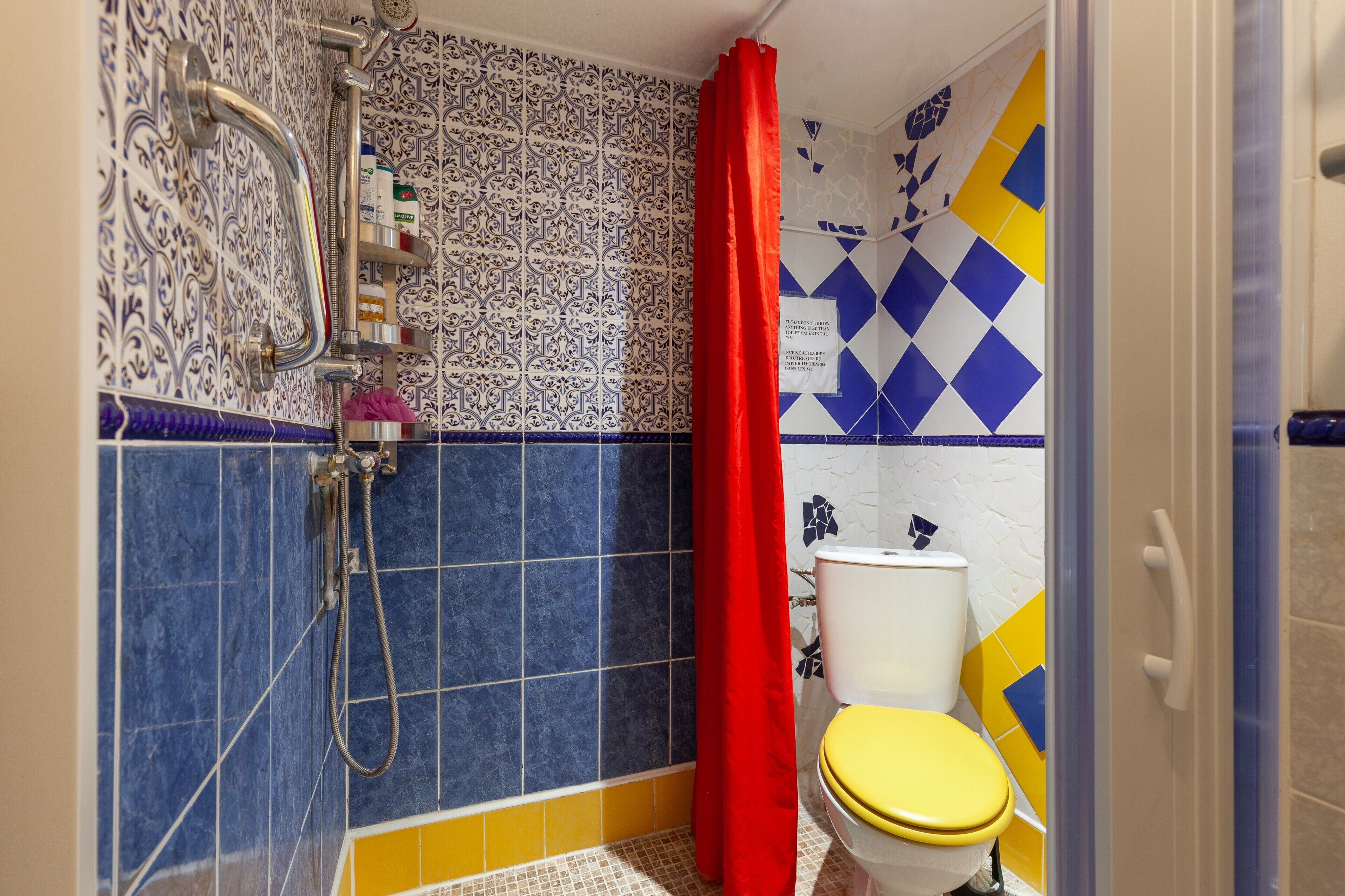 A bathroom with a shower, toilet, and a red curtain.