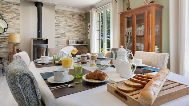 Een eethoek met een ontbijt gedekte tafel, inclusief croissants, brood en een theepot.