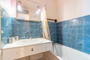 Une salle de bain avec un lavabo blanc, des murs recouverts de carreaux bleus, un rideau de douche et une étagère en verre au-dessus du lavabo.