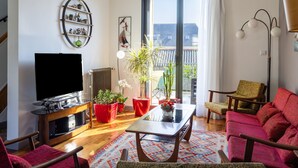 En stue med et fladskærms-tv, røde blomsterpotter, et træsofabord og en stor skydedør, der fører ud til en balkon.