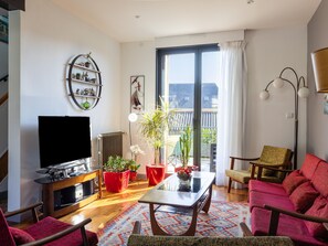 A living room with a flat-screen TV, red potted plants, a wooden coffee table, and a large sliding glass door leading to a balcony. - Villa Roz, 2–6 Guests, 100 m from the Port, Perros-Guirec (Perros Guirec)