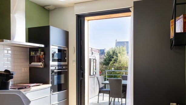 Et moderne køkken med indbygget ovn og mikroovn, et spiseområde med bord og stole, samt en skydedør til en udendørs terrasse.