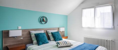 A bedroom with a bed, a nightstand, a wall-mounted lamp, a radiator, and a window.