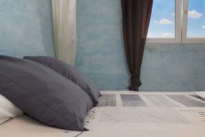 A bed with pillows, a patterned bedspread, a window with curtains, and a blue wall.