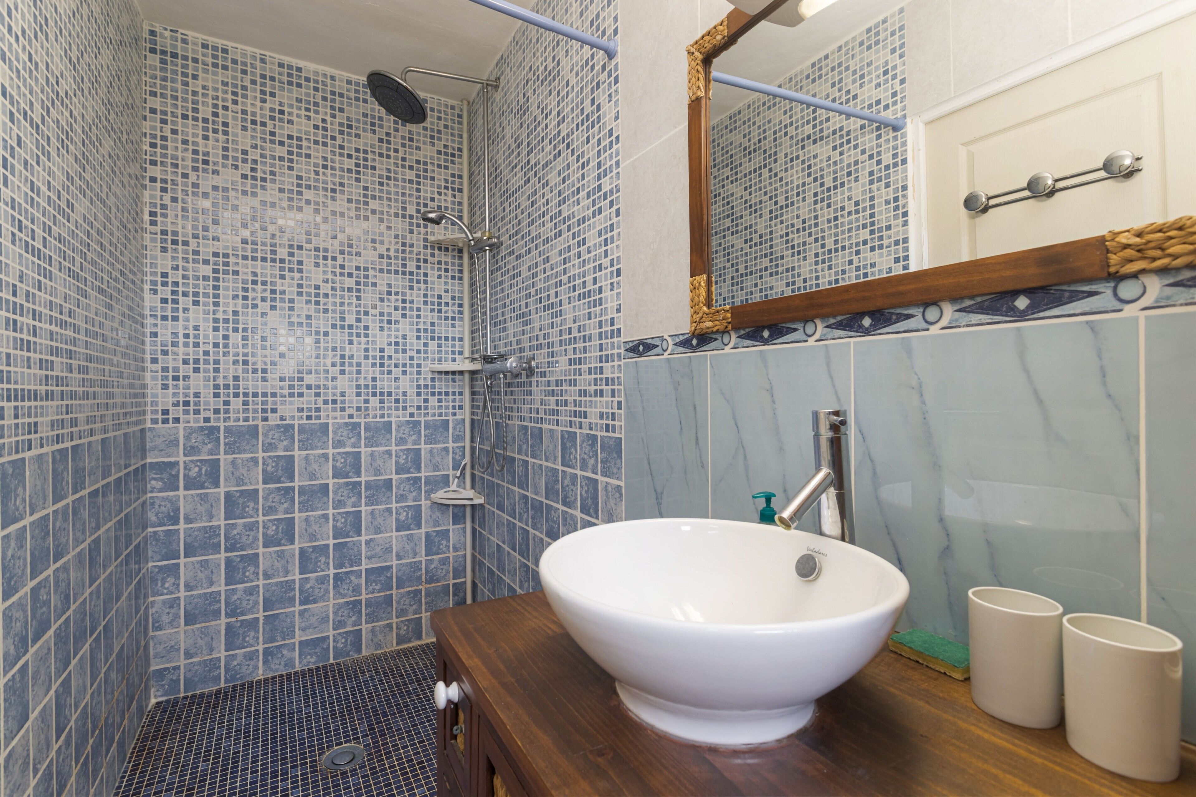 Ein Badezimmer mit einem weißen Waschbecken, einer Dusche inklusive Duschbrausehandstück und einem Spiegel mit Holzrahmen.