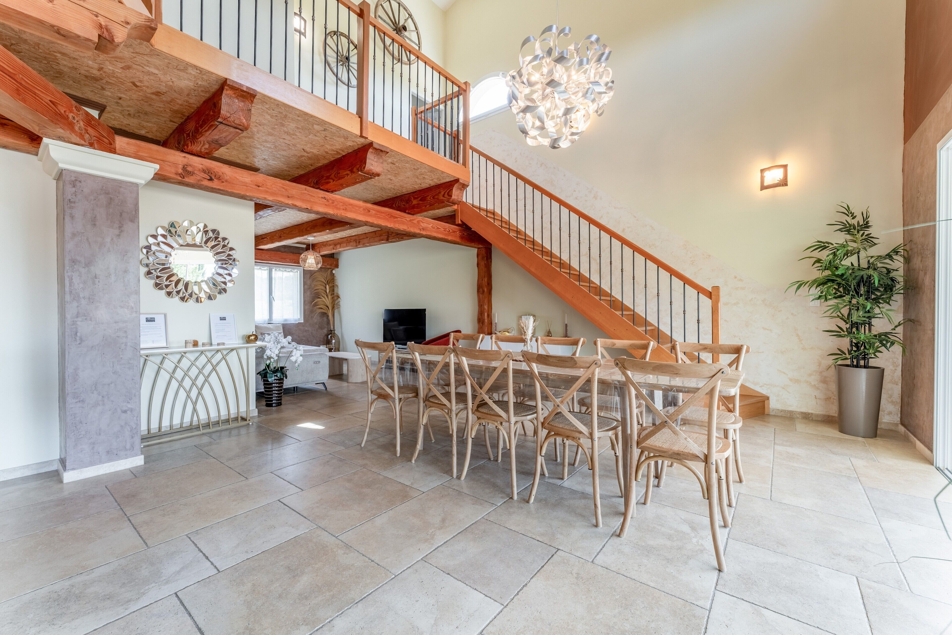 A spacious interior with a wooden staircase, a dining area with wicker chairs, and a large potted plant.