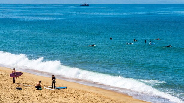 Une plage où l’on voit des surfeurs et, au loin, un navire.