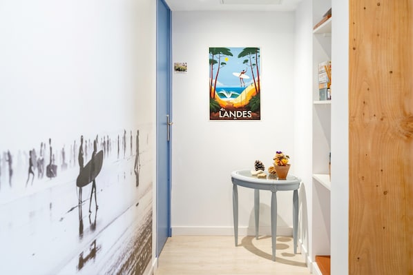 A hallway with a beach-themed poster, a small table with a vase, and a wooden door.
