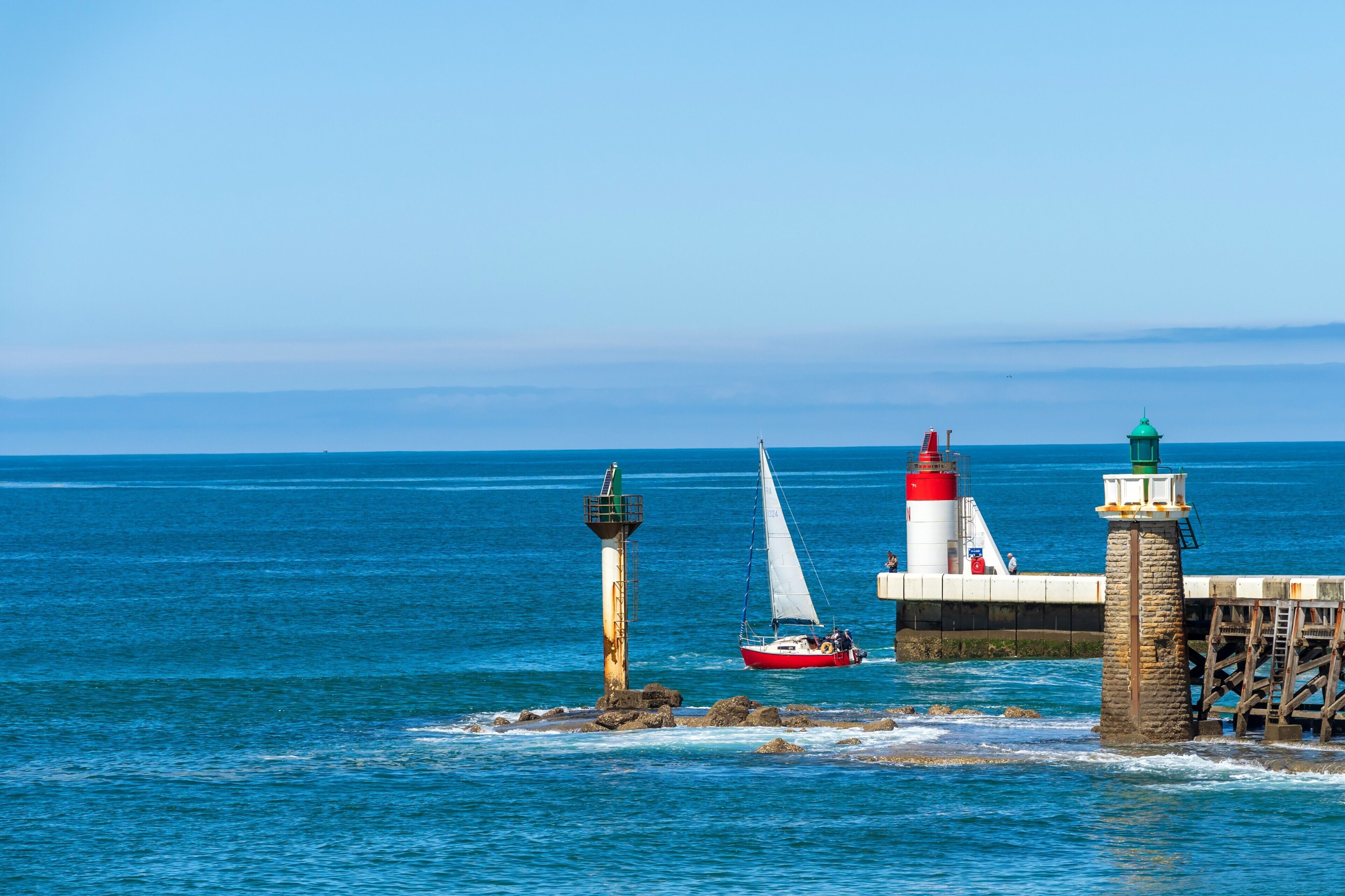 Un paysage côtier avec un phare, une jetée et un voilier.