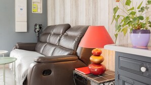 Ein Zimmer mit Ledersofa, roter Lampe, Zimmerpflanze, kleinem Tisch und Schrank.