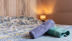 Ein Bett mit einem blumigen Überwurf, ein violettes Handtuch und ein grünes Handtuch.