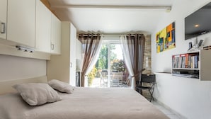 A bedroom with a bed, curtains, a TV, a bookshelf, and a view of the outdoors. - Guest Room "Chrisama" with Shared Pool, Wi-Fi, and Air Conditioning (Flayosc)