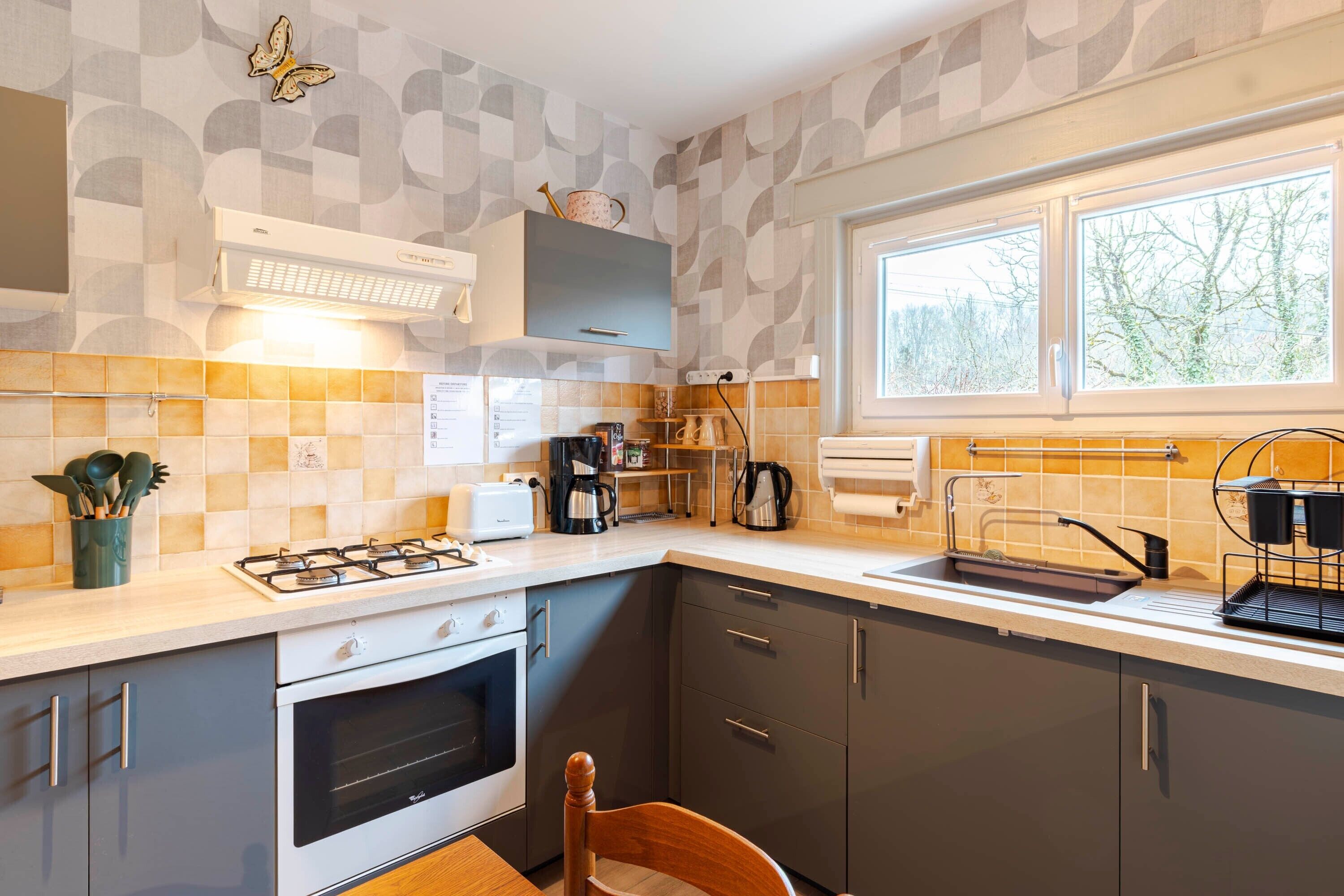 A modern kitchen with a gas stove, oven, and a window with a view of trees.