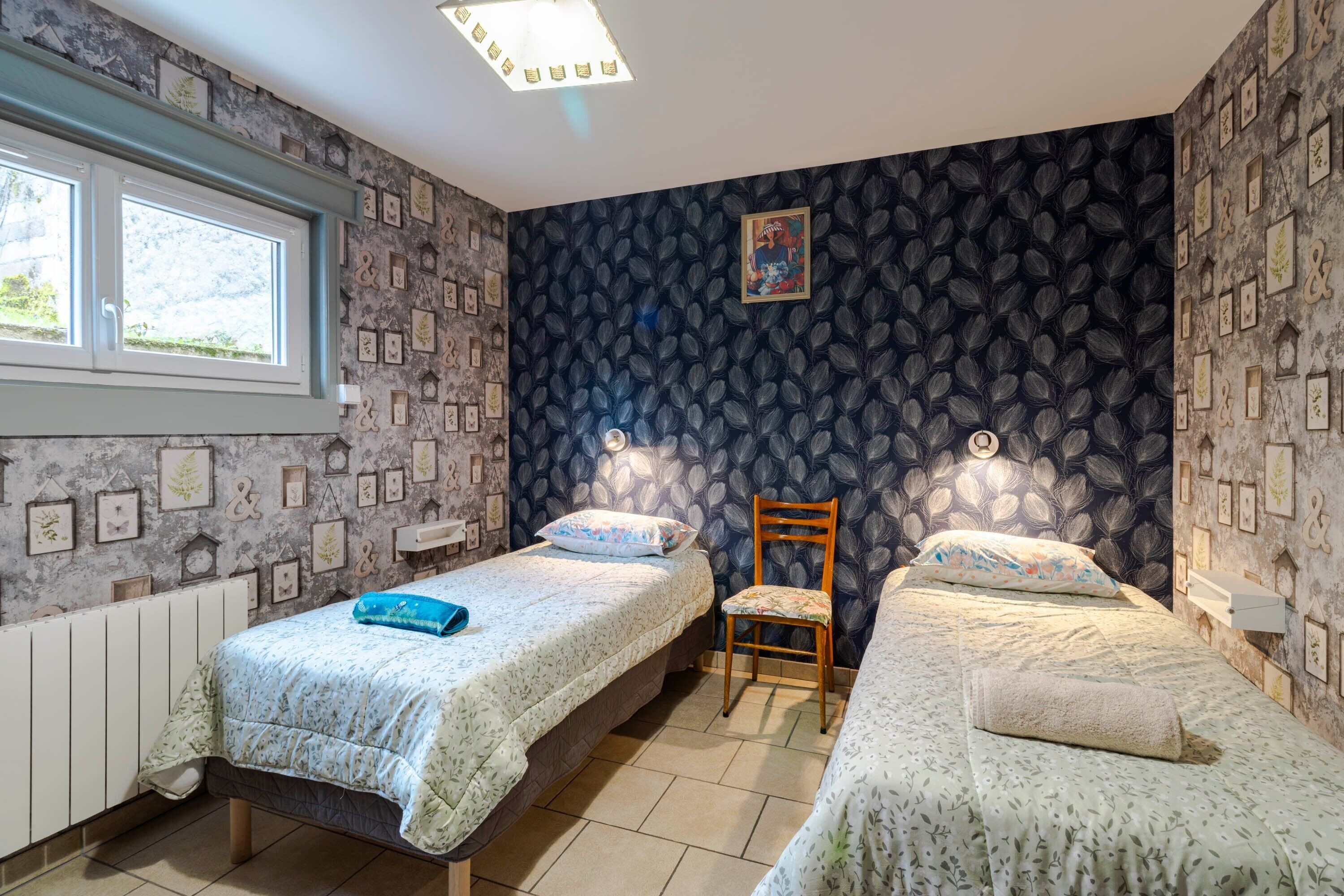 A room with two single beds, a chair, a radiator, a window, and a wall with framed pictures.