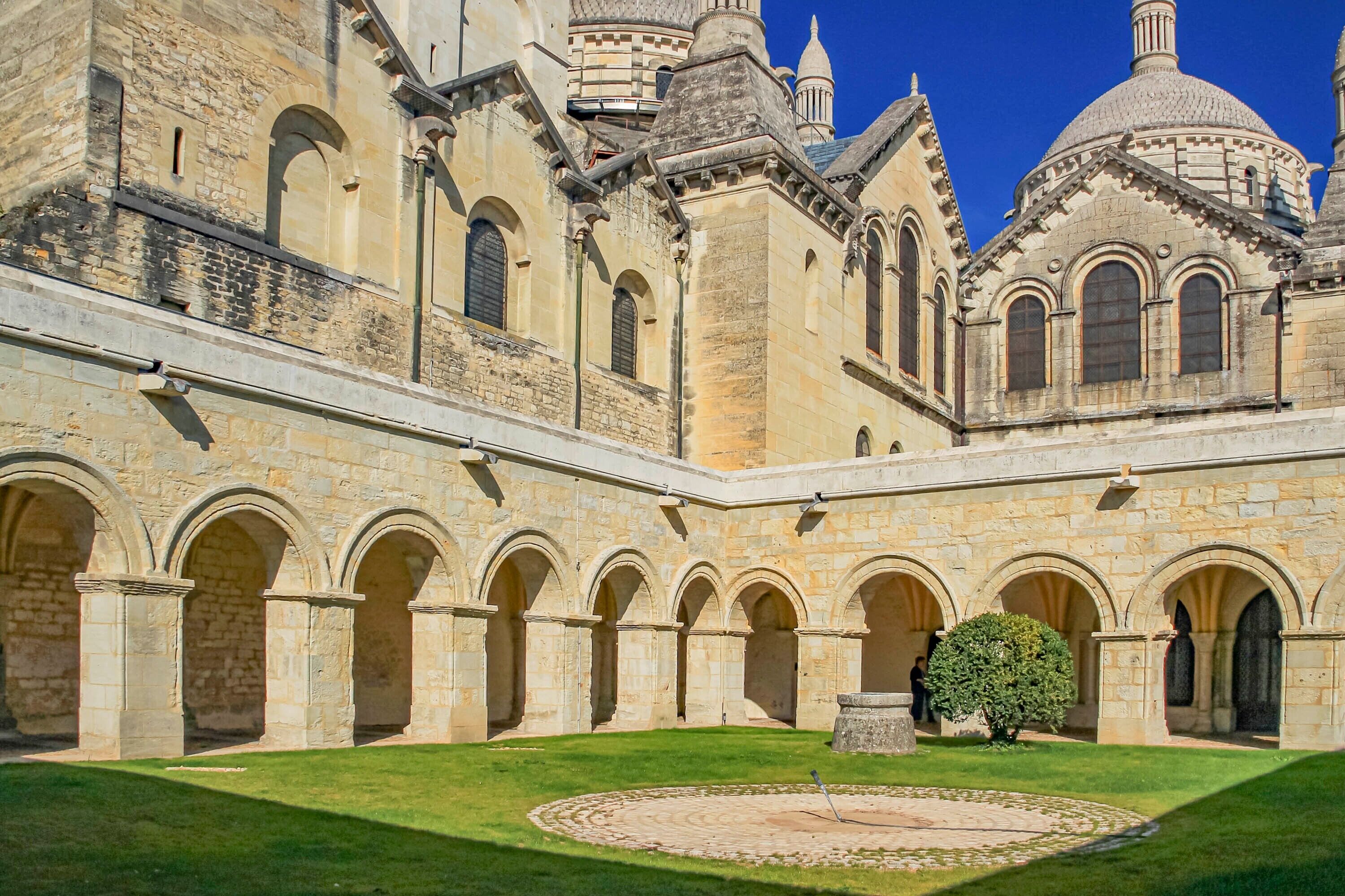 A courtyard with stone arches, a central circular area, and a building with domed and arched windows.