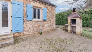 Une maison en pierre avec une allée gravillonnée, un petit four extérieur et une fenêtre avec des volets.