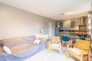Ein Wohnzimmer mit einer Couch, Sesseln, einem Tisch und einer Küche im Hintergrund.