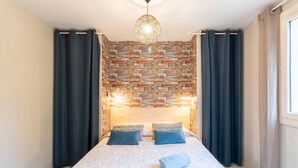 Une chambre à coucher avec une tête de lit ornée d’un motif en briques, un lit avec une literie blanche, deux oreillers et une serviette enroulée.