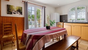 A room with a dining table, chairs, a bench, a window with curtains, a cabinet, and a painting on the wall. - Spacious House in the Heart of Médoc Between Estuary and Ocean (Bégadan)