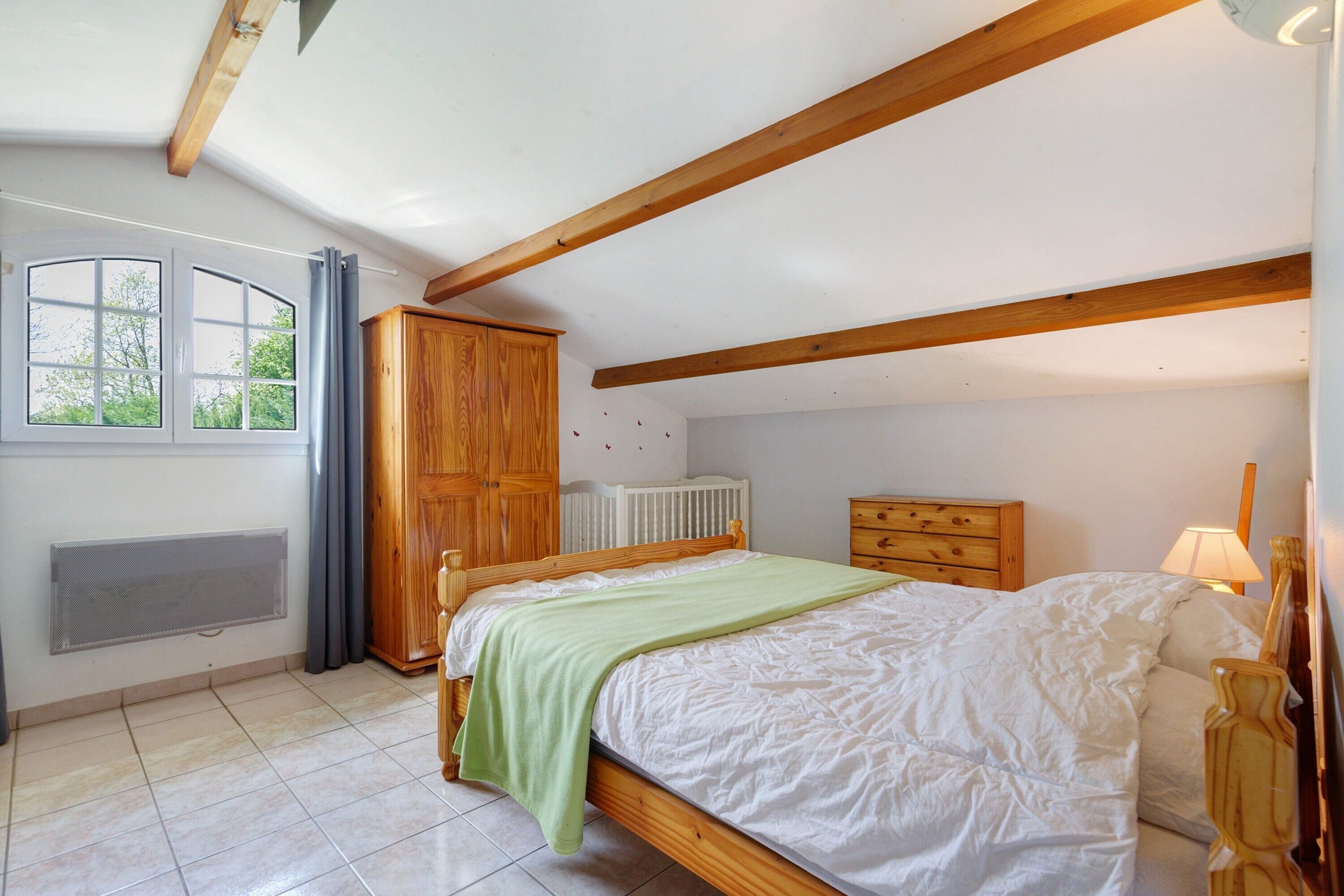 Een slaapkamer met een bed, een houten garderobe, een radiator en een raam met gordijnen.