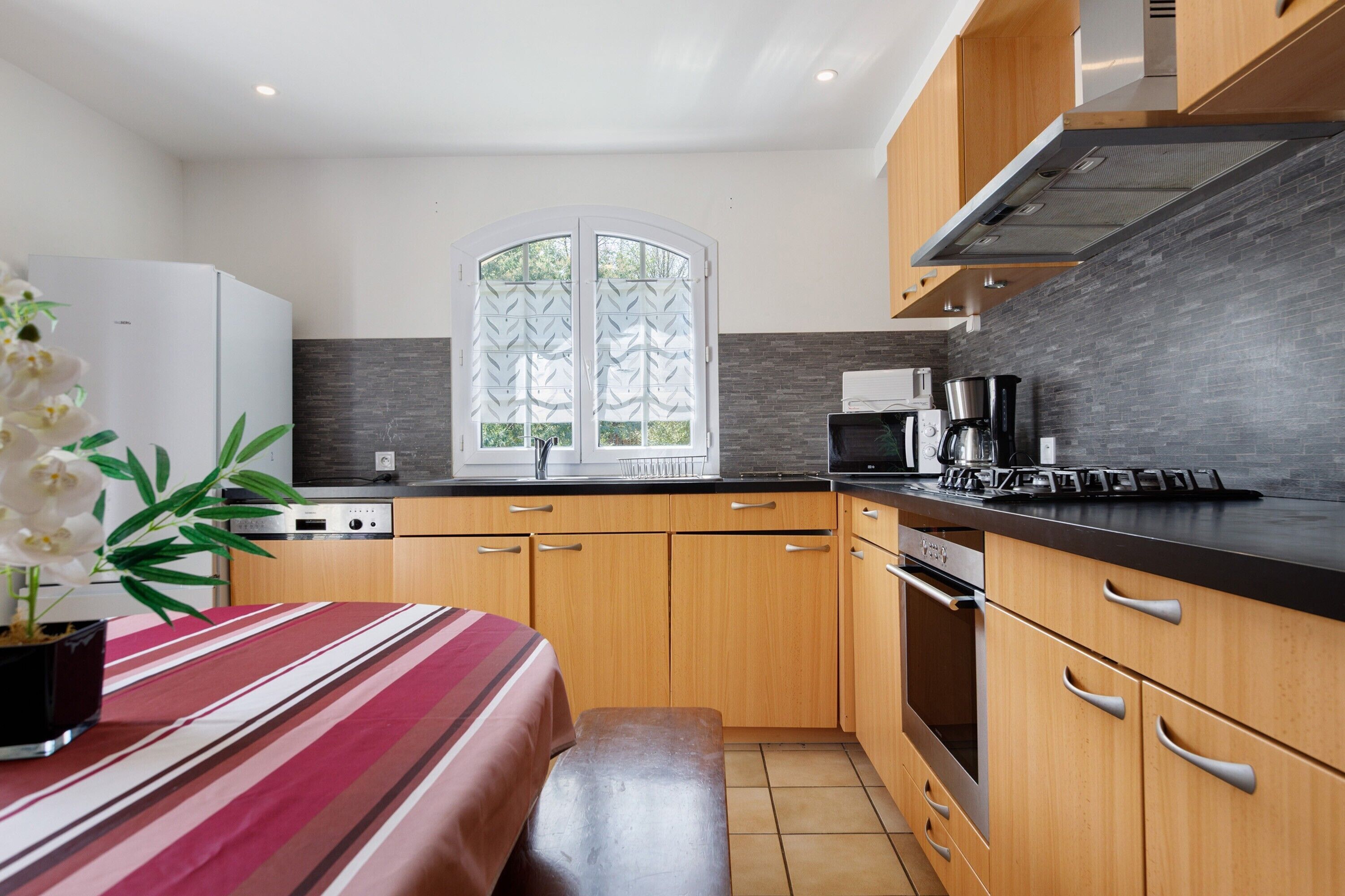 Una cocina moderna con armarios de madera, encimera negra y una ventana con detalles decorativos.