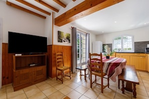 A room with a TV, wooden furniture, a dining table, and a kitchen area. - Spacious House in the Heart of Médoc Between Estuary and Ocean (Bégadan)
