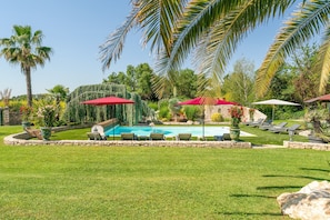 A backyard with a swimming pool, lounge chairs, and palm trees. - L'Oasis de Boisset: 5-Star Mas with Private Pool, Spa & Sauna (Boisset-et-Gaujac)