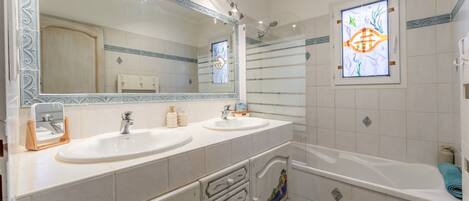 A bathroom with two sinks, a large mirror, a shower, and a decorative window.